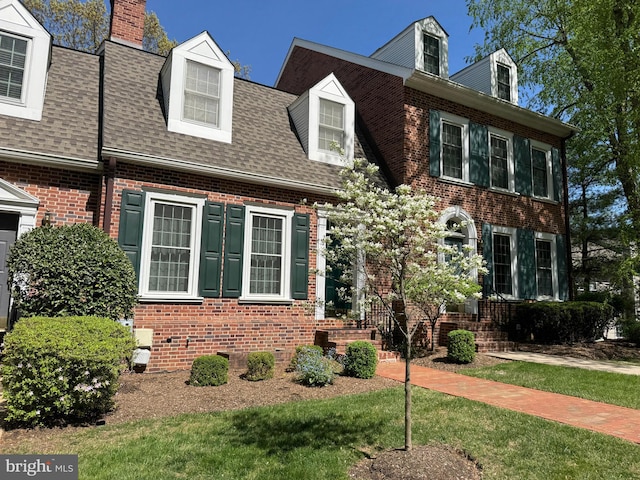 view of front of home featuring brick siding, a shingled roof, a front yard, and a chimney