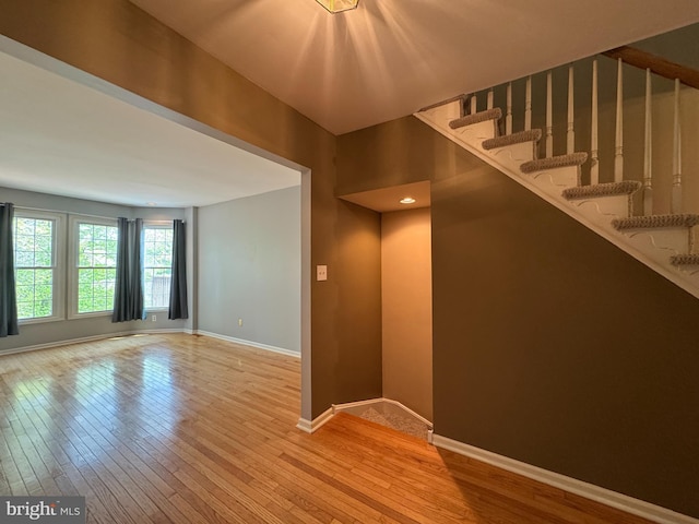 spare room featuring light wood-style floors, baseboards, and stairs