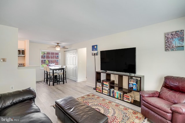living area with baseboards, ceiling fan, and light wood-type flooring