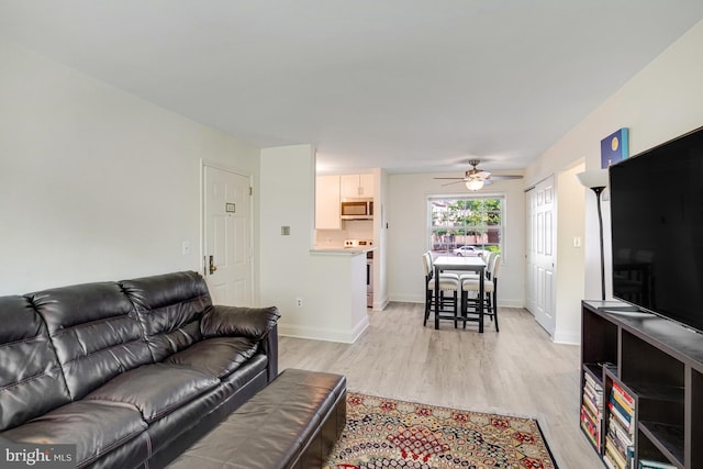living room featuring ceiling fan, baseboards, and light wood finished floors