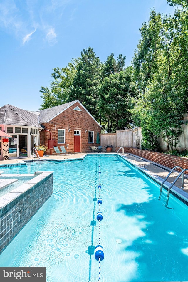 community pool featuring a fenced backyard, a patio, a jacuzzi, and an outbuilding