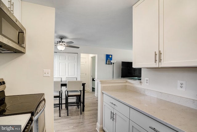 kitchen with a ceiling fan, light stone countertops, light wood-type flooring, stainless steel appliances, and white cabinetry