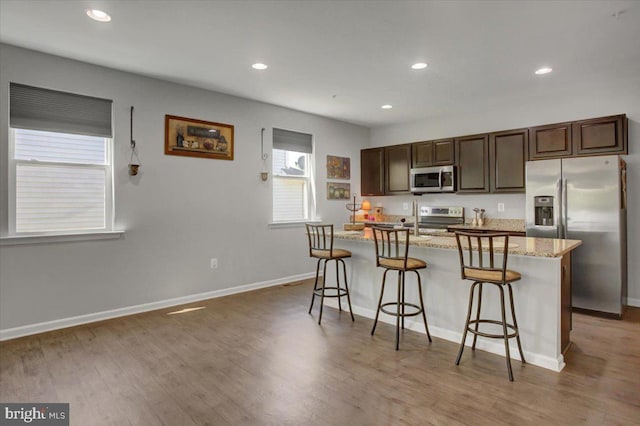 kitchen with light wood-style floors, appliances with stainless steel finishes, dark brown cabinetry, and a kitchen breakfast bar