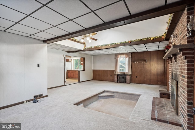 basement featuring a ceiling fan, carpet, a brick fireplace, and wooden walls