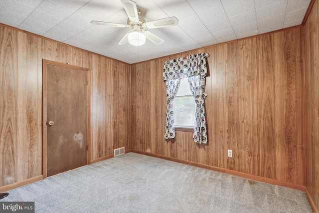 empty room featuring ceiling fan, carpet, wood walls, and visible vents