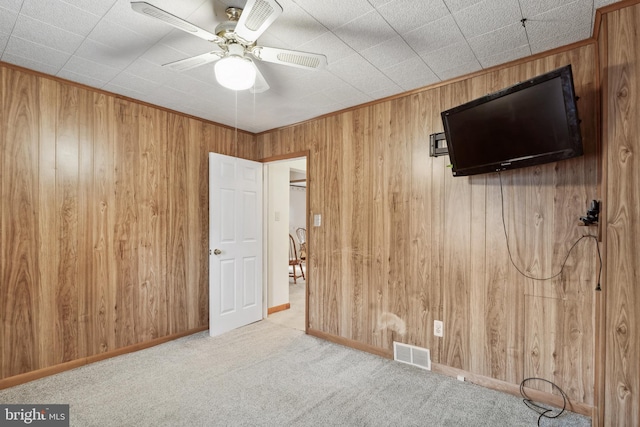 unfurnished bedroom with ceiling fan, visible vents, baseboards, wooden walls, and carpet flooring
