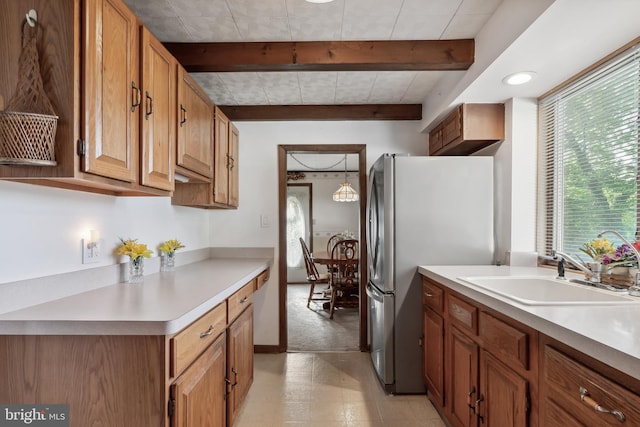 kitchen featuring a sink, beam ceiling, freestanding refrigerator, and light countertops
