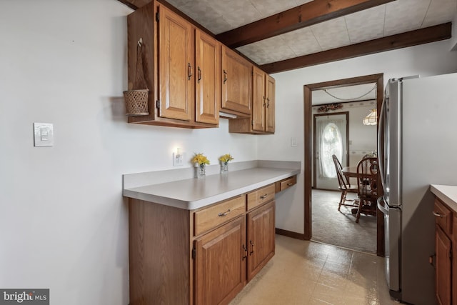 kitchen featuring light countertops, freestanding refrigerator, brown cabinetry, and beamed ceiling