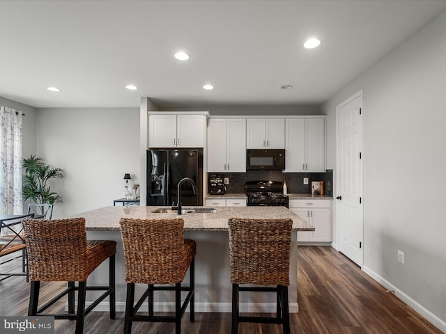 kitchen featuring tasteful backsplash, a sink, a kitchen island with sink, a kitchen bar, and black appliances