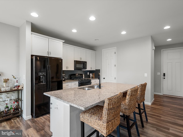 kitchen with backsplash, dark wood-style flooring, a center island with sink, a sink, and black appliances