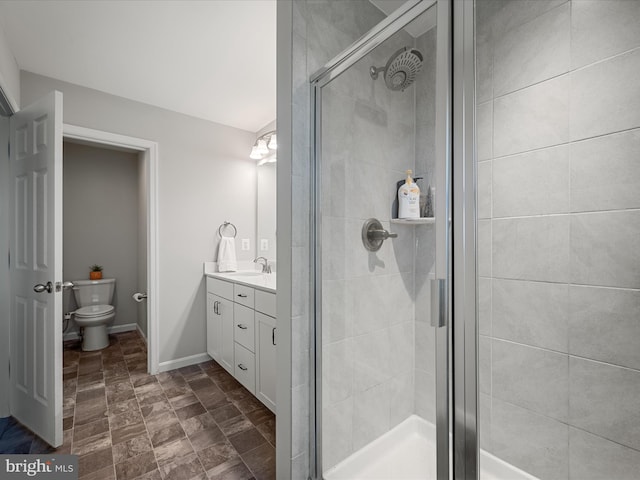 full bath with stone finish floor, a stall shower, vanity, baseboards, and toilet
