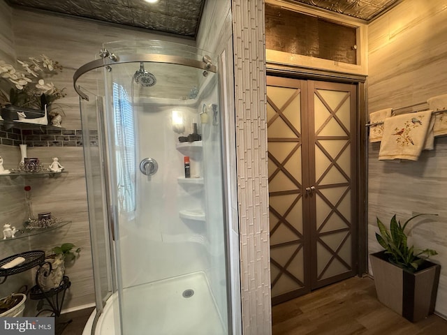 bathroom with wood finished floors, wood walls, and a stall shower