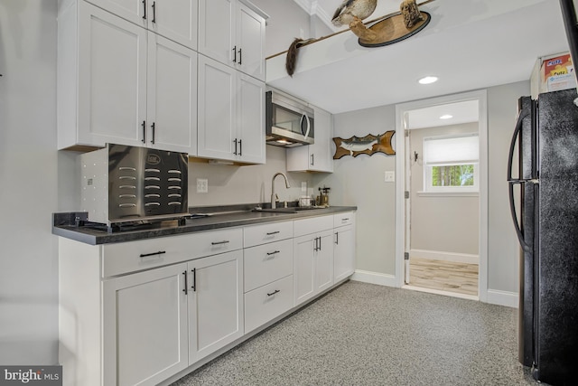 kitchen with freestanding refrigerator, baseboards, stainless steel microwave, a sink, and white cabinetry