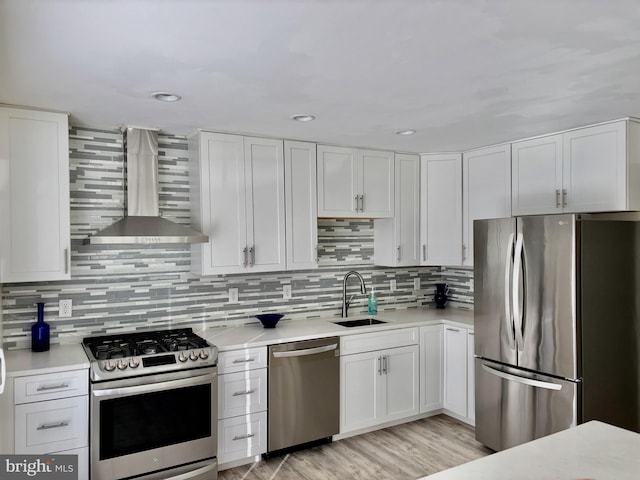 kitchen featuring light countertops, wall chimney exhaust hood, white cabinets, a sink, and appliances with stainless steel finishes