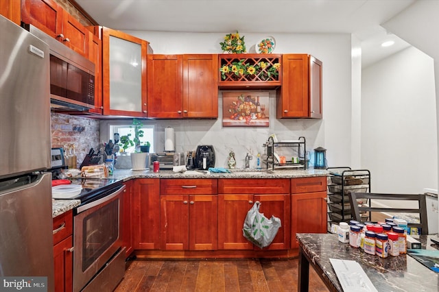 kitchen featuring light stone counters, decorative backsplash, stainless steel appliances, and dark wood-style floors