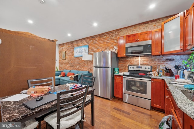 kitchen featuring brown cabinets, light stone countertops, brick wall, light wood-style flooring, and stainless steel appliances