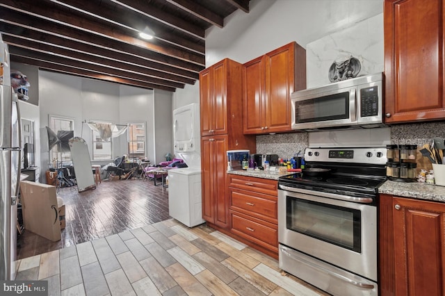kitchen with appliances with stainless steel finishes, tasteful backsplash, stacked washer / drying machine, beam ceiling, and a high ceiling