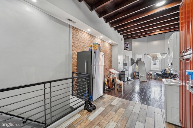 interior space with visible vents, freestanding refrigerator, wood finished floors, brick wall, and wood ceiling