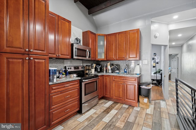 kitchen with light stone countertops, appliances with stainless steel finishes, a sink, light wood finished floors, and tasteful backsplash