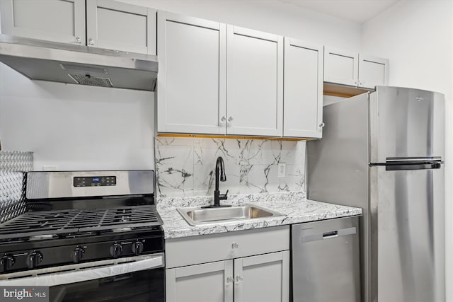 kitchen featuring decorative backsplash, under cabinet range hood, light stone counters, a sink, and appliances with stainless steel finishes