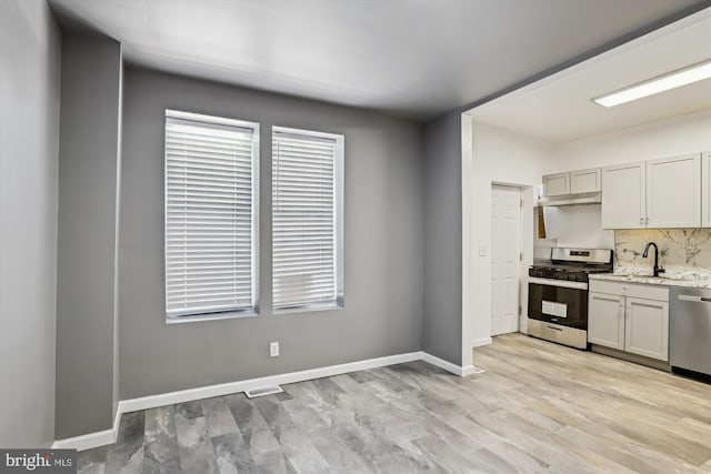 kitchen with light stone counters, a sink, stainless steel appliances, tasteful backsplash, and under cabinet range hood