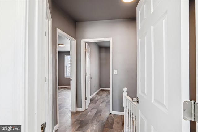 hallway featuring baseboards, an upstairs landing, and dark wood-style floors