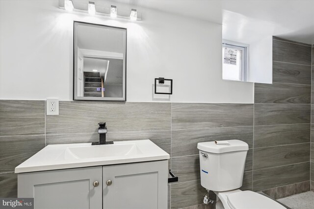 bathroom with toilet, tile walls, and vanity