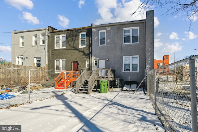snow covered rear of property with a fenced backyard, stairway, a chimney, and cooling unit