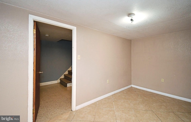 empty room featuring stairway, baseboards, a textured ceiling, and light tile patterned flooring
