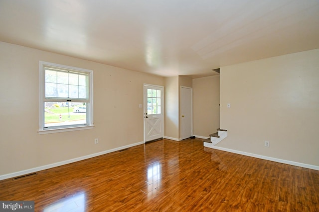 empty room with stairs, baseboards, visible vents, and wood finished floors