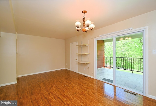 unfurnished room with an inviting chandelier, baseboards, wood finished floors, and visible vents