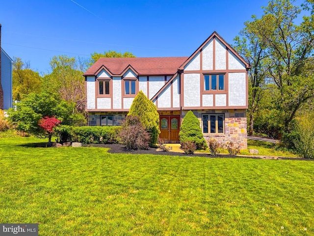 tudor-style house with a front lawn, stucco siding, and stone siding