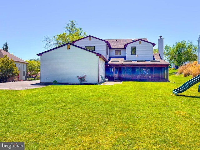 back of property featuring a lawn, roof with shingles, a chimney, and a playground
