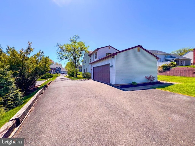 exterior space with fence, a residential view, an attached garage, and aphalt driveway