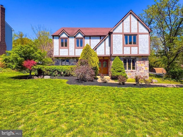 tudor-style house featuring a front yard, french doors, stone siding, and stucco siding