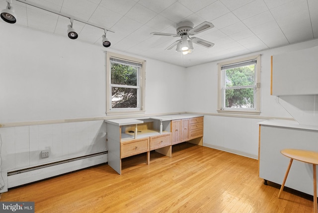unfurnished bedroom featuring track lighting, a baseboard radiator, light wood-style floors, and wainscoting