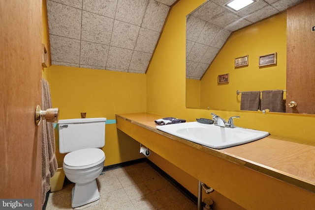 half bathroom with toilet, tile patterned floors, vaulted ceiling, and a sink