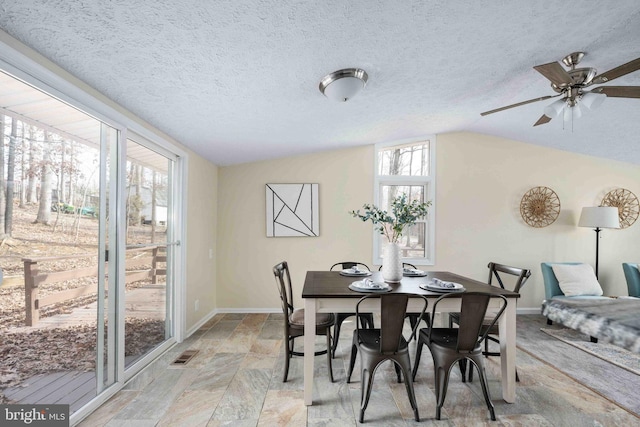 dining space with visible vents, stone tile floors, lofted ceiling, baseboards, and ceiling fan