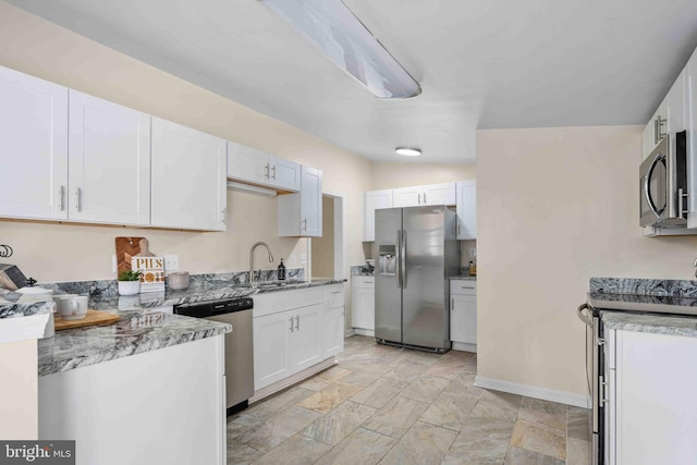 kitchen with baseboards, white cabinets, a sink, stone finish flooring, and stainless steel appliances