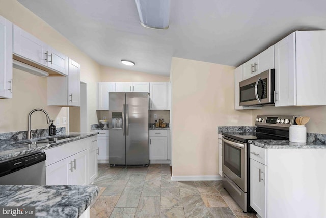 kitchen featuring appliances with stainless steel finishes, a sink, white cabinets, lofted ceiling, and stone counters