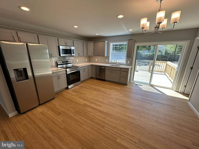 kitchen with backsplash, appliances with stainless steel finishes, gray cabinetry, light countertops, and an inviting chandelier