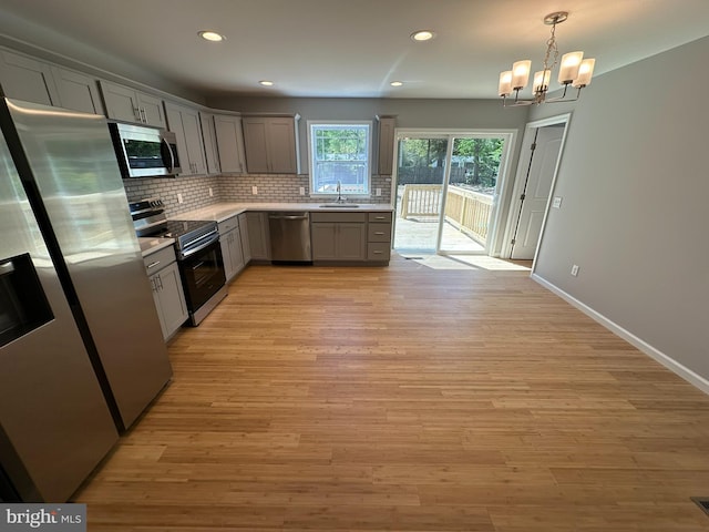 kitchen featuring gray cabinets, backsplash, appliances with stainless steel finishes, a sink, and a chandelier