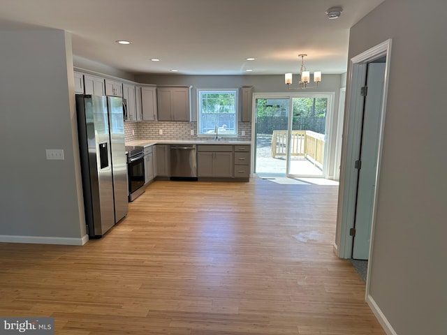 kitchen with gray cabinets, an inviting chandelier, a sink, light wood-style floors, and stainless steel appliances