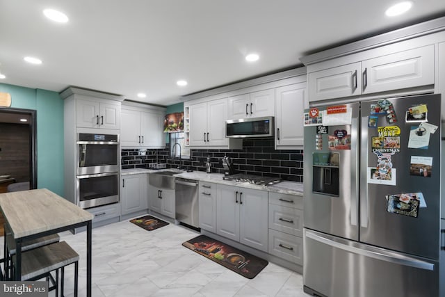 kitchen with appliances with stainless steel finishes, a sink, marble finish floor, tasteful backsplash, and gray cabinetry