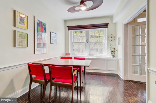 dining space featuring dark wood-type flooring, a ceiling fan, a decorative wall, and a wainscoted wall