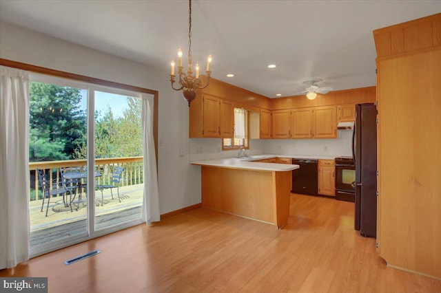 kitchen featuring a peninsula, light countertops, under cabinet range hood, light wood-style flooring, and black appliances