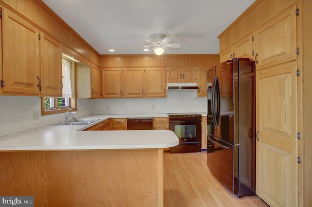 kitchen featuring a sink, light wood-style flooring, a peninsula, under cabinet range hood, and black appliances