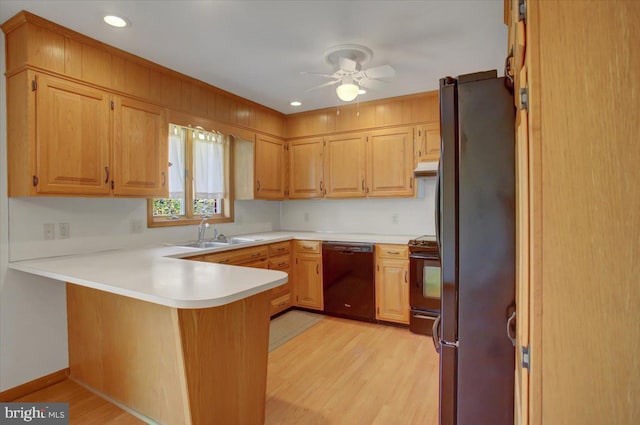 kitchen featuring a ceiling fan, a sink, black appliances, light wood finished floors, and a peninsula