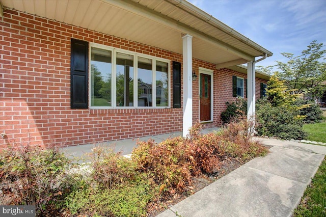 entrance to property featuring a porch and brick siding