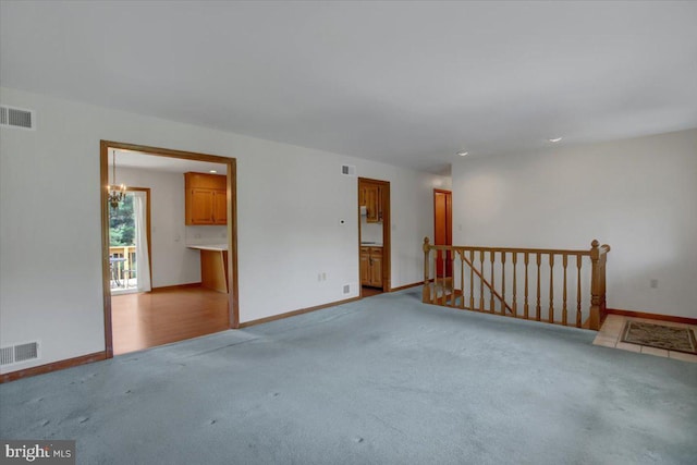 carpeted empty room featuring baseboards, visible vents, and an inviting chandelier